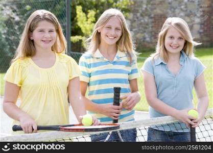 Three young girl friends with rackets on tennis court smiling