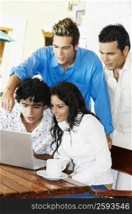 Three young men and a teenage girl using a laptop