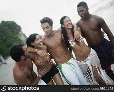 Three young men and two young women standing together on the beach and smiling