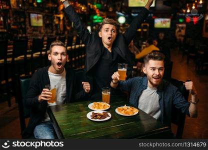 Three young men celebrates game victory in a sport bar, happy friendship of football fans