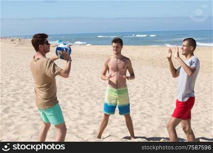 three young men having fun on the beach playing volleyball