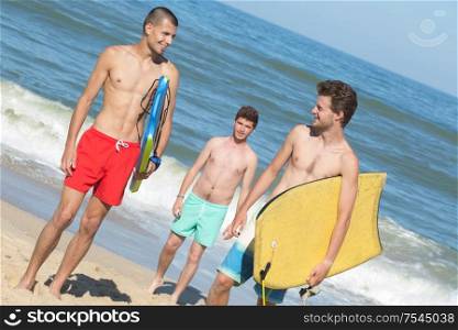 three young men on beach holding bodyboards