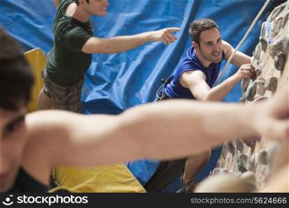 Three young men point and climbing in an indoor climbing gym