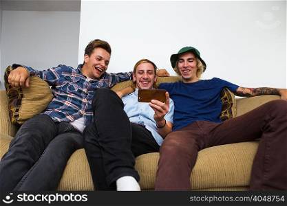 Three young men sitting on sofa, looking at smartphone