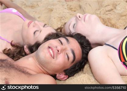 Three young people lying in the sand