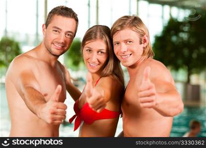 Three young people - woman and two men - at a public swimming pool standing in front of the water