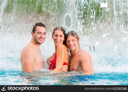 Three young people - woman and two men - at a public swimming pool standing under a water gadget