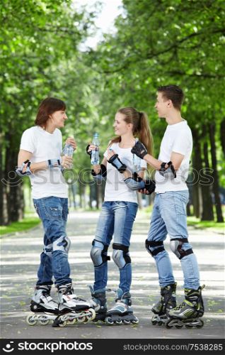 Three young skaters are drinking water in the park