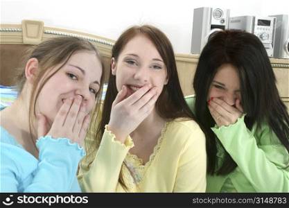 Three young teen girls in pajamas sitting in bed laughing.