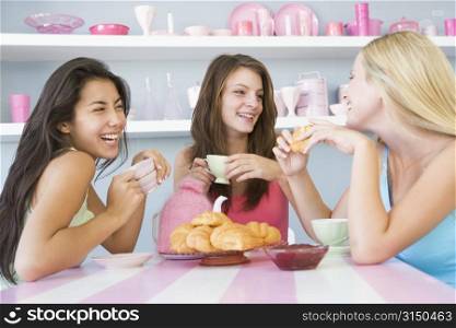 Three young woman sitting at a table having tea and a snack