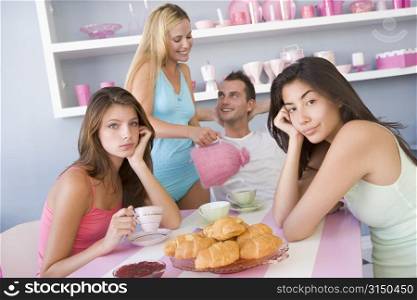 Three young women and a man sitting at a table having tea