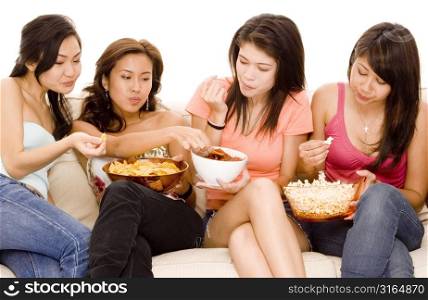 Three young women and a teenage girl sitting on a couch and eating snacks