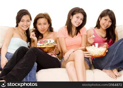 Three young women and a teenage girl sitting on a couch and eating snacks