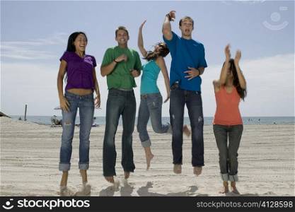 Three young women and two young men jumping on the beach