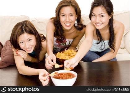 Three young women dipping chips into a bowl of salsa