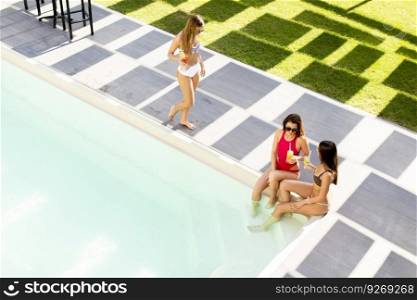 Three young women drinking coctails and having fun by swimming pool at hot summer day