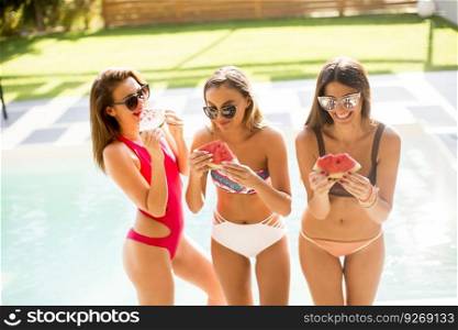 Three young women eating  watermelon by the pool at sunny day