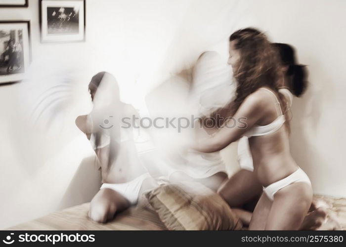 Three young women having a pillow fight on the bed