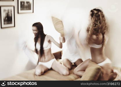 Three young women having a pillow fight on the bed