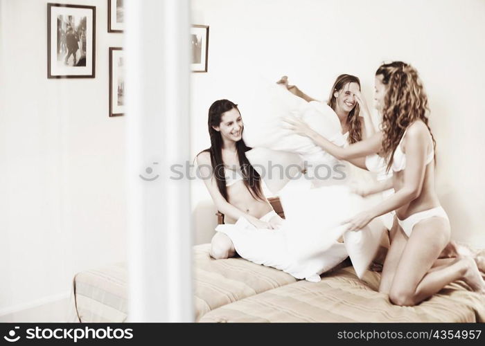 Three young women having a pillow fight on the bed