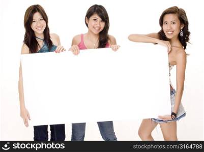 Three young women holding a blank placard and smiling