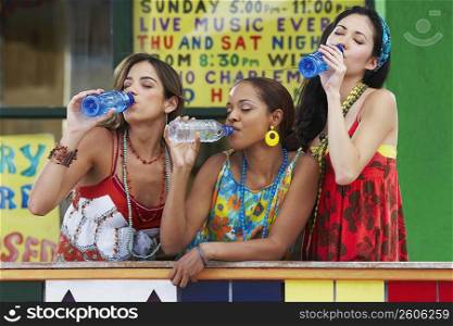 Three young women leaning on a railing and drinking water from bottles
