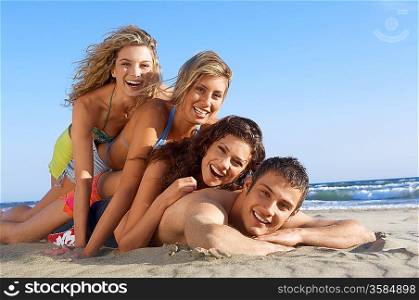 Three young women lying on man on beach, portrait, ground view