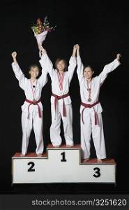 Three young women raising their hands on a winners podium
