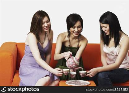Three young women sitting on a couch with tea cups