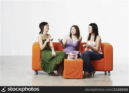 Three young women sitting on a couch with tea cups