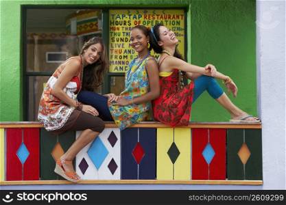 Three young women sitting on a railing and smiling