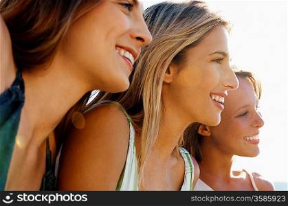 Three young women sitting side by side looking at view close up head and shoulders