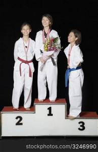 Three young women standing on a winners podium with their medals