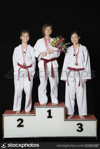 Three young women standing on a winners podium with their medals and smiling