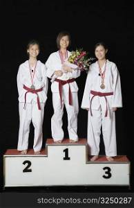 Three young women standing on a winners podium with their medals and smiling