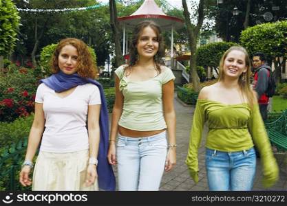 Three young women walking on a walkway in a park