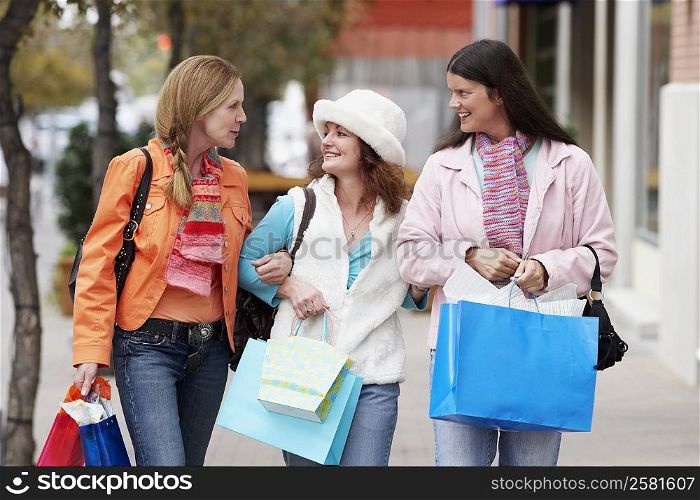 Three young women walking on footpath and carrying shopping bags