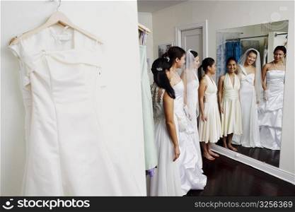 Three young women wearing wedding dresses and looking at themselves in a mirror