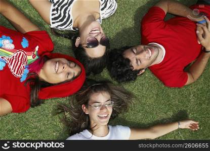 Three young women with a young man lying on grass and smiling