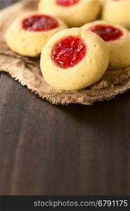 Thumbprint Christmas cookies filled with strawberry jam, photographed with natural light (Selective Focus, Focus on the lower edge of the jelly filling on the first cookie)