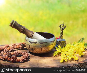 Tibetan copper singing bowl and rosary on wooden stump in the rays of the sun