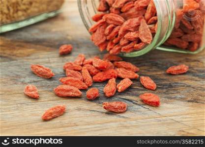 Tibetan goji berries (wolfberry) spilling of the glass jar on a wooden surface, selective focus