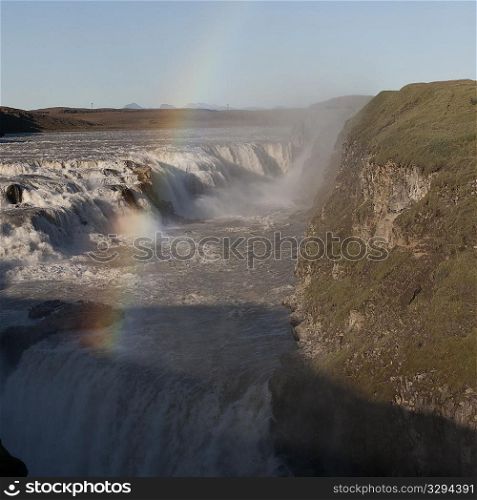 Tiered waterfall with grassed cliff and rainbow