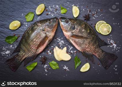 Tilapia fish freshwater and ginger lemon lime herb spices vegetable for cooking food in the asian restaurant / Fresh raw tilapia on black background