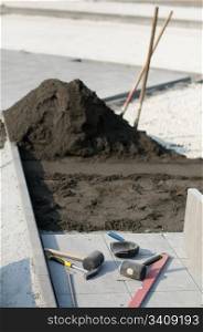 Tiling of pavement and sand pile. Two shovels and Construction tools scattered