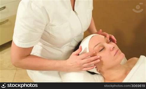 Tilt and dolly shot of a professional cosmetician making a facial massage with accent on eye area