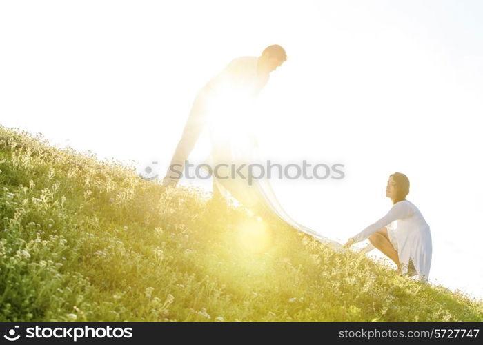 Tilt image of young couple spreading picnic blanket on grass during sunny day