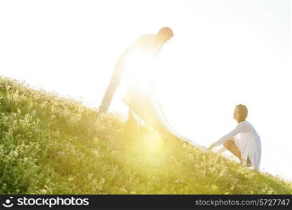 Tilt image of young couple spreading picnic blanket on grass during sunny day