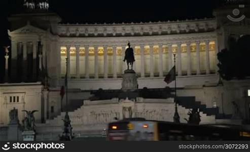 Tilt shot of a woman coming up to the road and taking a picture of Altar of Fatherland at night. Female tourist using touch pad to capture landmarks of Rome