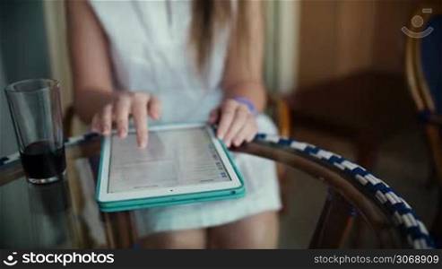 Tilt shot of a woman sitting at the table on the hotel balcony. She using tablet PC, having refresher and enjoying summer day